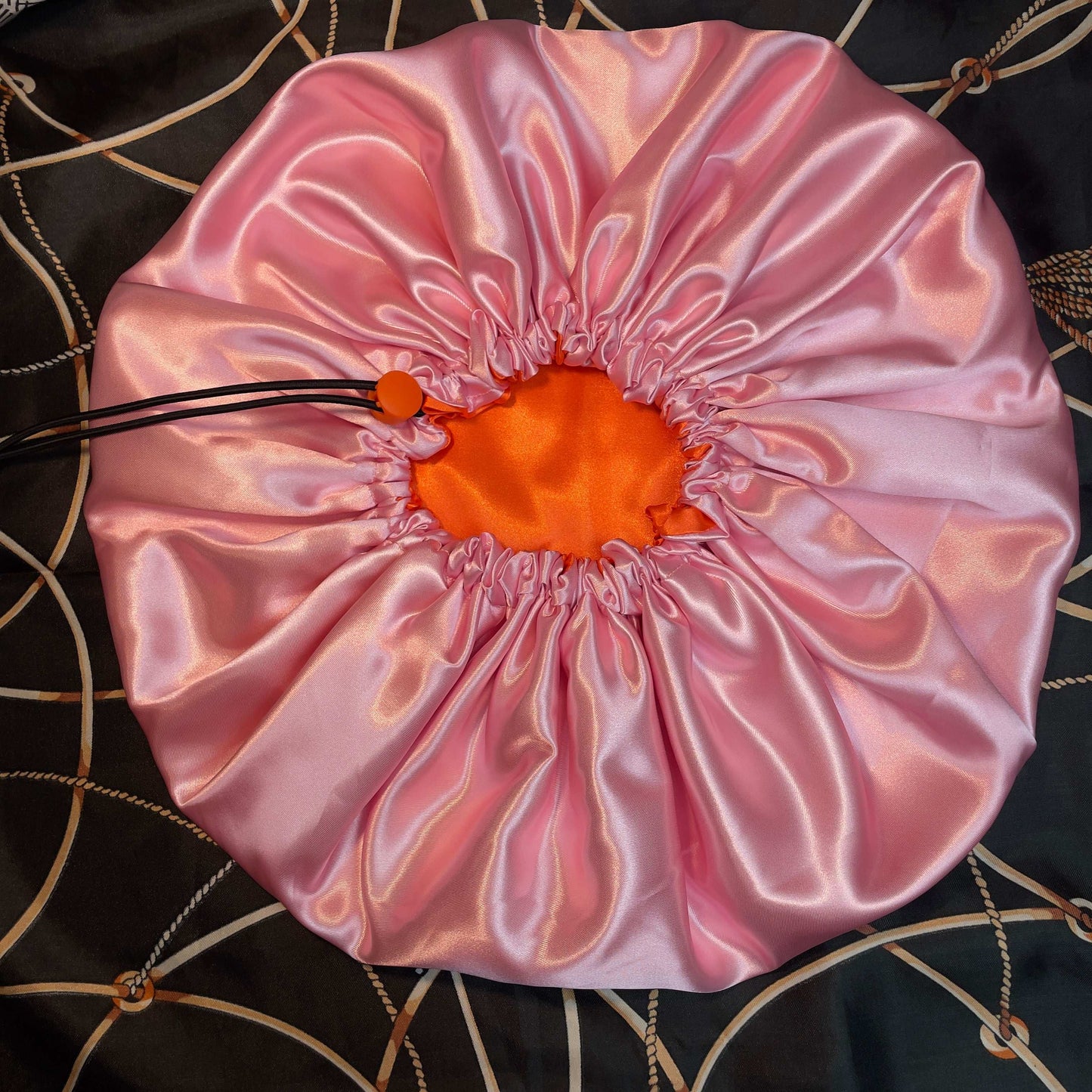 Pink satin drawstring bonnet with orange center on a decorative background