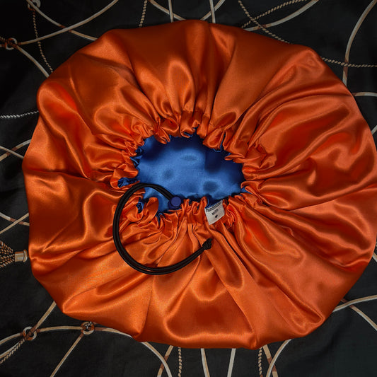 Orange satin drawstring bonnet with a blue interior on a patterned fabric background