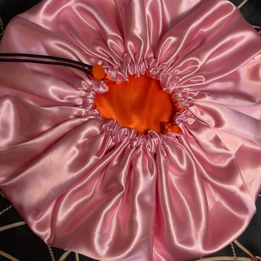 Pink satin drawstring bonnet with orange center on a black and white patterned surface