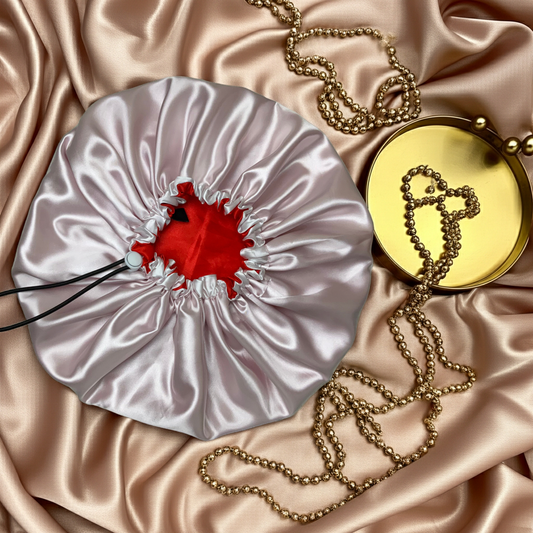 White satin bag with red interior, gold chain, and yellow round object on pink satin fabric