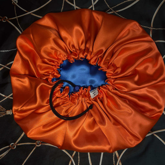 Orange satin drawstring bonnet with a blue interior on a patterned fabric background