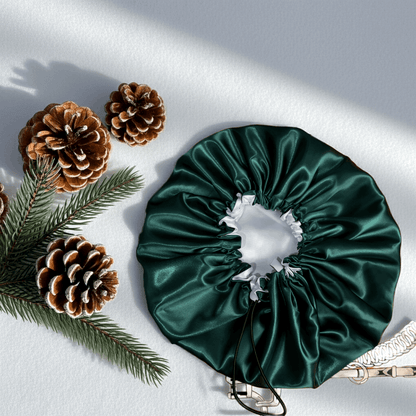 Green satin bonnet with decorative bow, pine cones, and branches on a light background