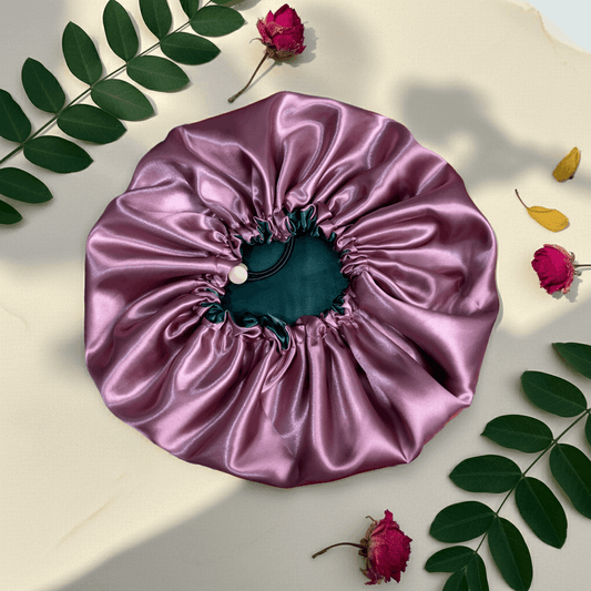 Pink satin hair bonnet on a light background with leaves and flowers