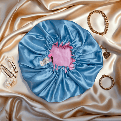 Blue satin hair bonnet with pink interior on a satin surface with jewelry.