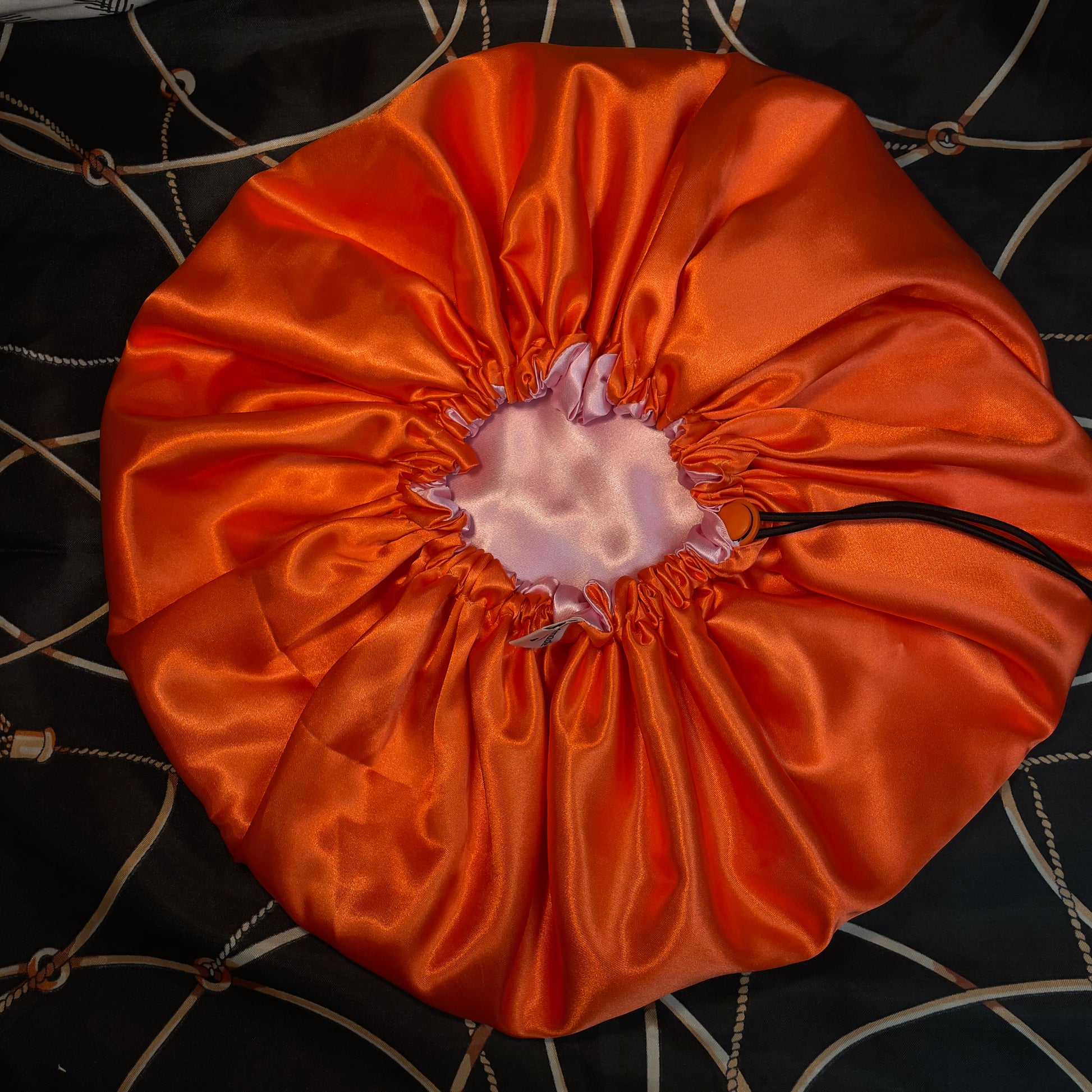 Orange satin drawstring bonnet on a textured black and gold surface