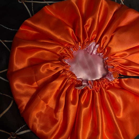 Orange satin hair bonnet with a pink interior on a dark background
