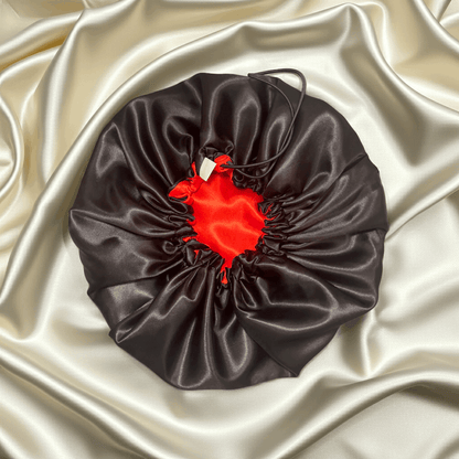 Black satin drawstring bag with a red heart-shaped object on a beige satin background