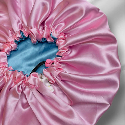 Close-up view of a reversible satin drawstring bonnet in pink and blue colors, showing the double-layered fabric and adjustable drawstring.