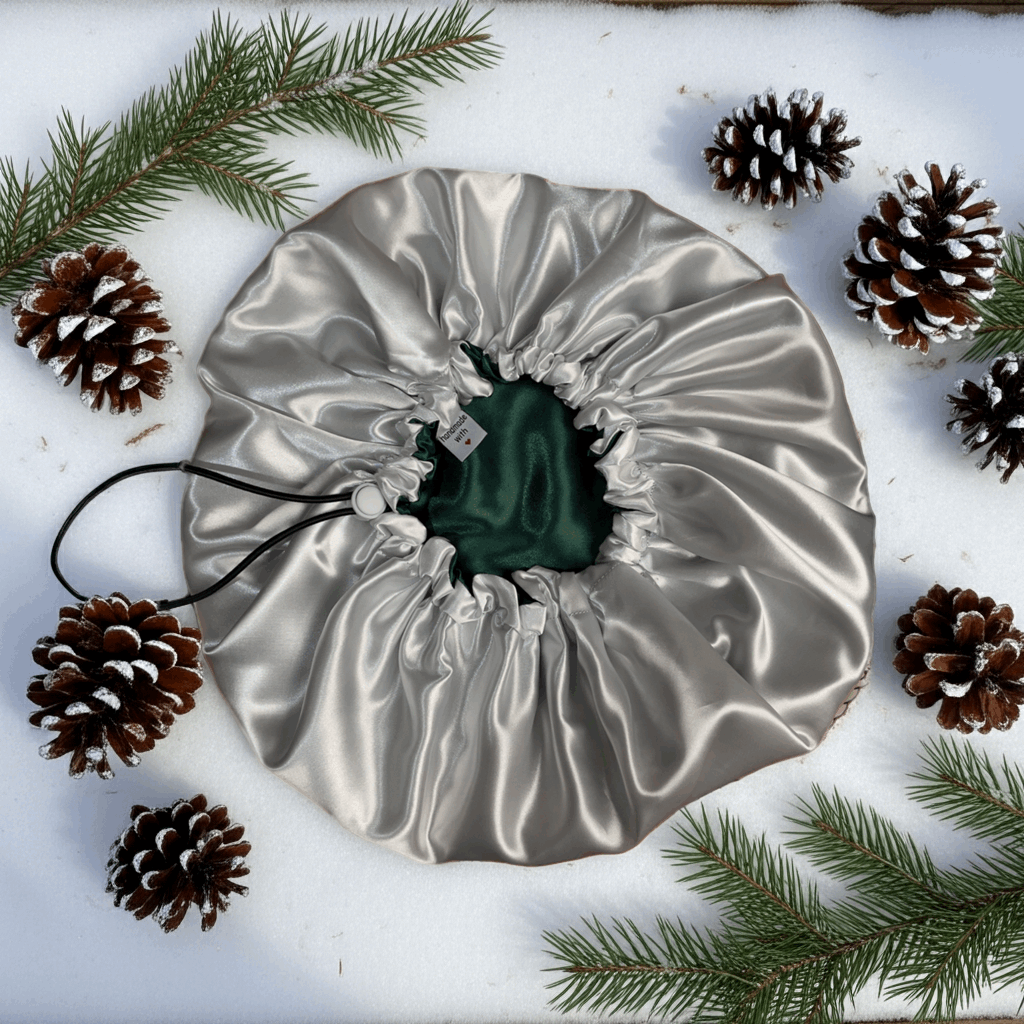 Silver drawstring bag with a green item inside, surrounded by pine cones and branches on a white background
