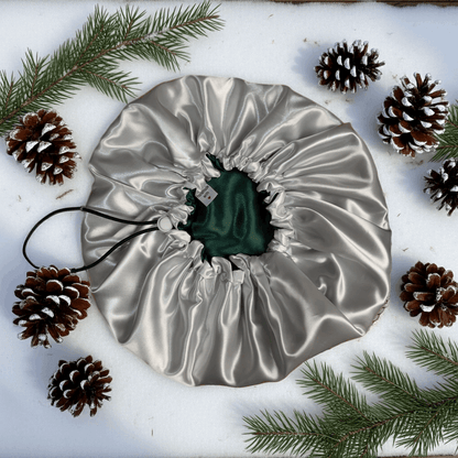 Silver drawstring bag with a green item inside, surrounded by pine cones and branches on a white background