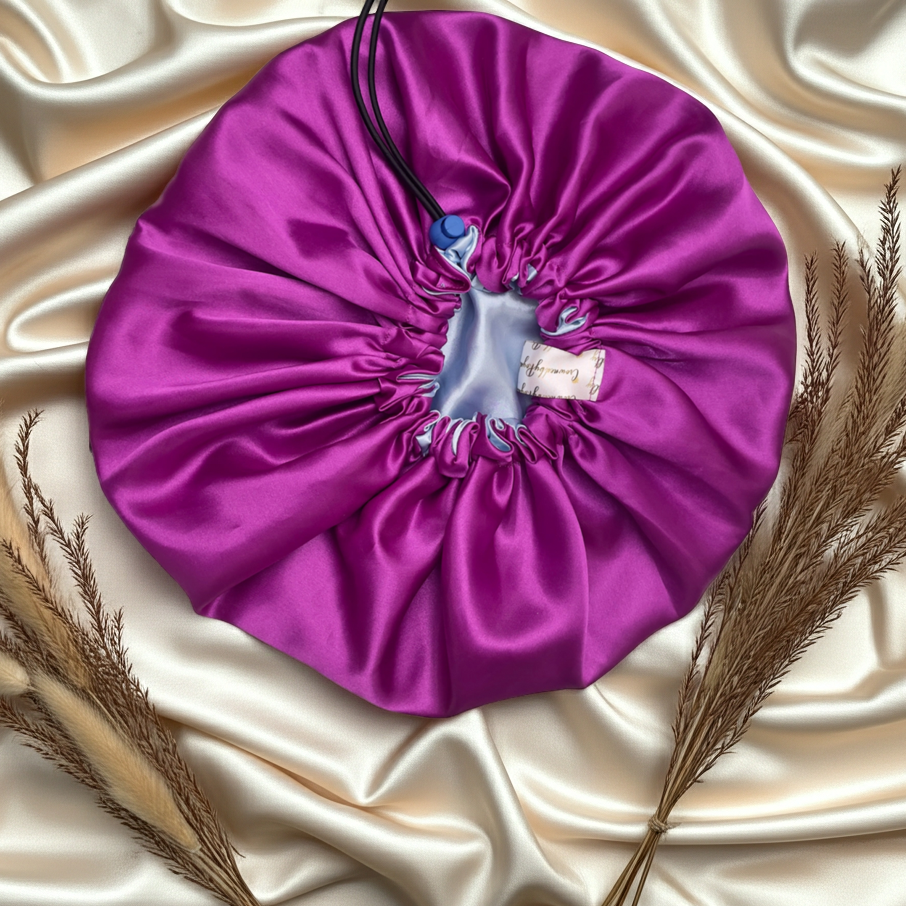 Purple drawstring bag on a textured beige surface with dried plants.