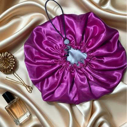 Purple satin drawstring bonnet on a beige satin surface with a perfume bottle and hair accessories.
