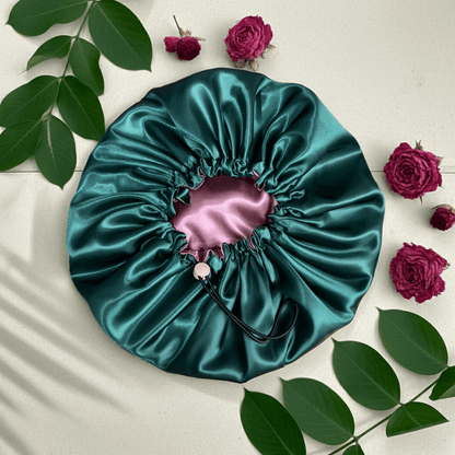 Teal satin drawstring bag with pink interior on a light surface with green leaves and red roses.