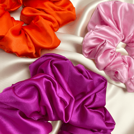 Three colorful satin scrunchies on a light fabric background