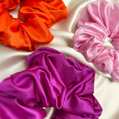 Three colorful satin scrunchies on a light fabric background