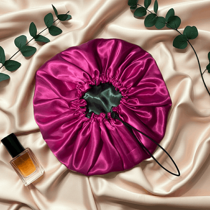 Pink satin drawstring bag on a beige fabric background with a bottle of perfume and green leaves.