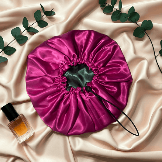 Pink satin drawstring bag on a beige fabric background with a bottle of perfume and green leaves.