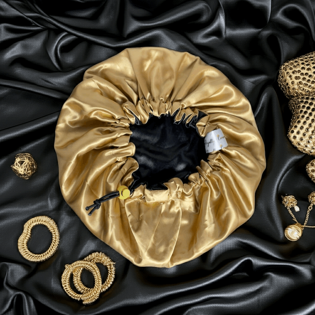 Gold satin drawstring bag on black satin fabric with gold jewelry items.