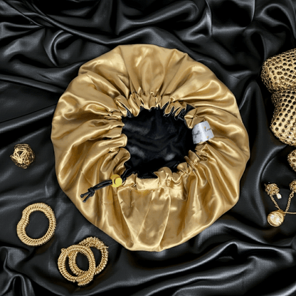 Gold satin drawstring bag on black satin fabric with gold jewelry items.