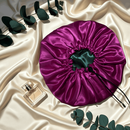 Purple satin drawstring bag on a beige fabric background with a perfume bottle and green leaves.