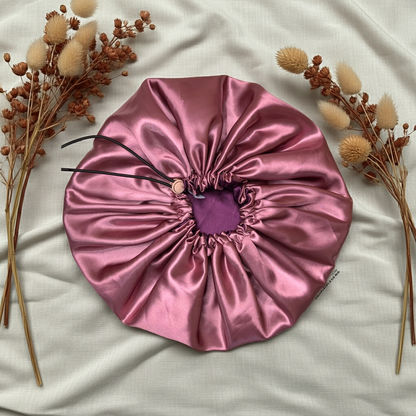 Pink satin hair bonnet on a light fabric background with dried flowers.